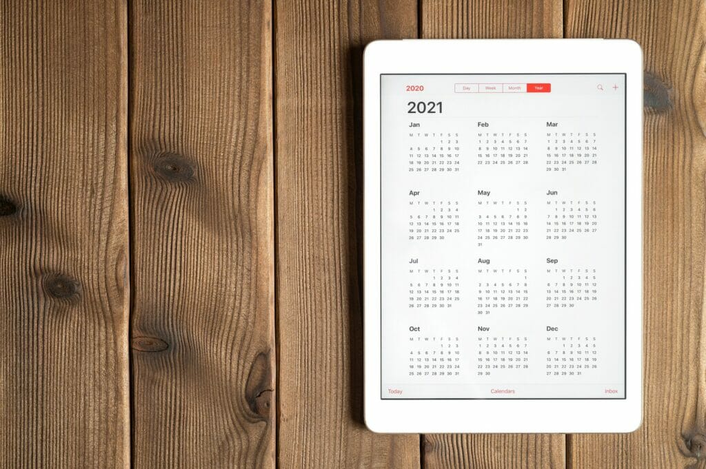 a tablet with an open calendar for 2021 year on a wooden boards table background. space for text.