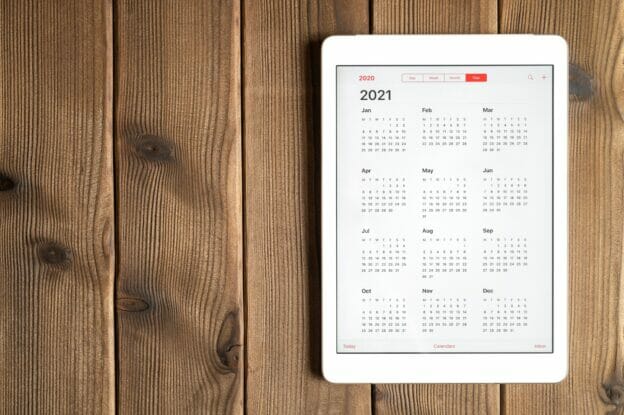a tablet with an open calendar for 2021 year on a wooden boards table background. space for text.