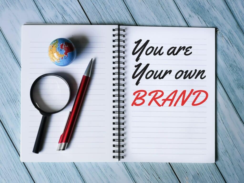Selective focus notebook written you are your own brand with pen,mini globe and magnifying glass.