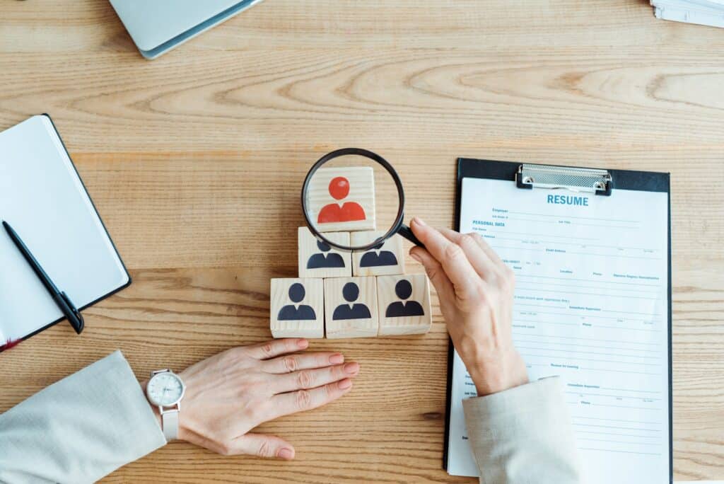 top view of recruiter holding magnifier near cube and clipboard in office