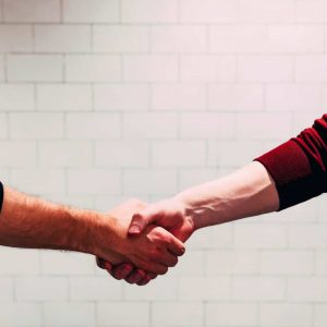 Photo by Chris Liverani two person shaking hands near white painted wall